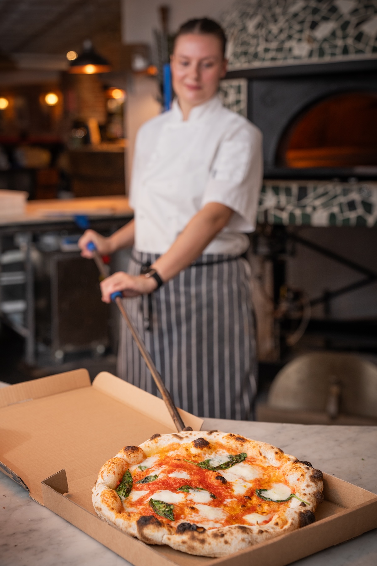 A skilled chef at Pizza on the Park prepares a traditional Neapolitan-style pizza, freshly baked for office catering in Bristol. Featuring an open kitchen setup, this image showcases the quality and authenticity behind each pizza, making it a perfect catering option for offices in Clifton. Businesses looking for fresh, high-quality pizza made with local ingredients will find Pizza on the Park a reliable catering solution for office parties, corporate events, and team lunches.