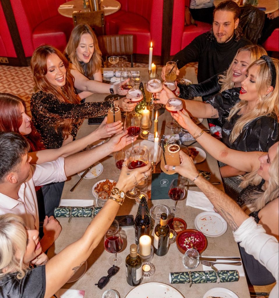 A group of friends toasts over an elegant spread of pizza, cocktails, and wine at Pizza on the Park. The festive table, illuminated by candles, makes this the perfect venue for group Christmas meals and office Christmas parties in Bristol.